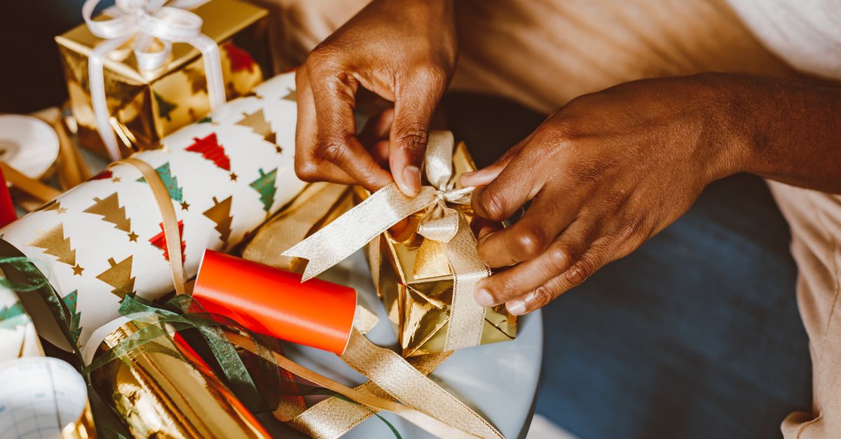 Hands tying ribbons on Christmas gifts with festive wrapping paper and gold accents.
